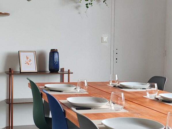 Ein Essbereich mit einem Holztisch, gedeckt für vier Personen, umgeben von Stühlen. Über dem Tisch befindet sich ein Regal mit einem gerahmten Bild und einer Vase.