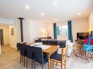 Ein modernes Wohnzimmer mit Essbereich, Kamin, Fernseher und einem großen Fenster mit Vorhängen.