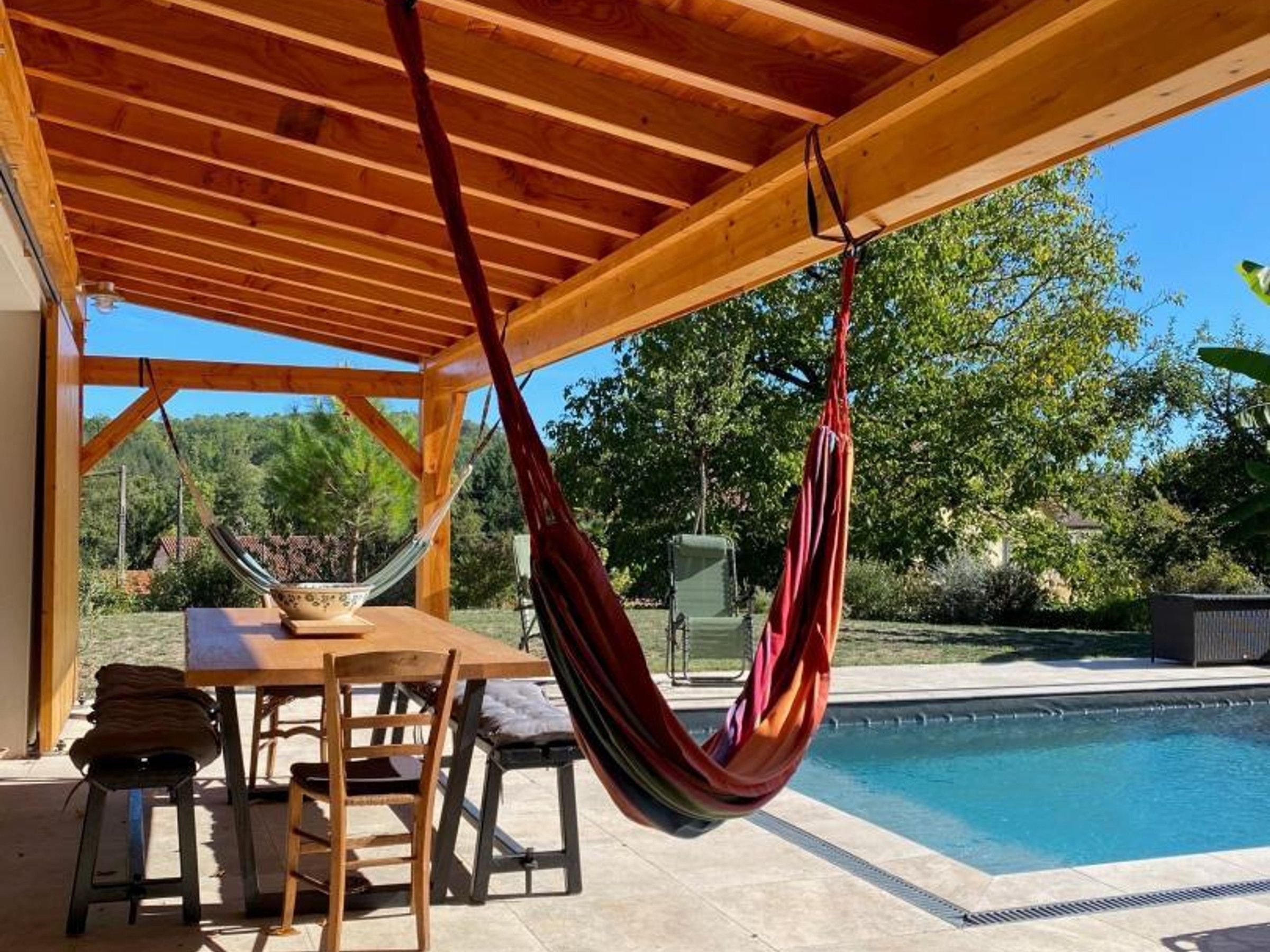 Une pergola en bois avec un hamac, une piscine et une table avec des chaises.