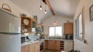 Una cocina con armarios de madera, un refrigerador, una ventana y una mesa de comedor con un cesto de piñas.