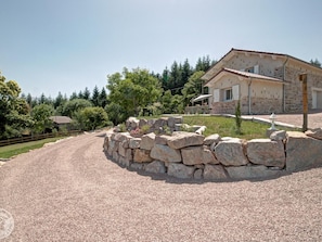 A stone house with a gravel driveway, surrounded by trees and a stone wall.