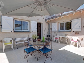 An outdoor patio with a round table and chairs, a large umbrella, and a rustic building with stone walls and windows.