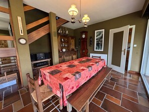 Een eetruimte met een lange tafel, stoelen, een houten trap, een klok en een kast.