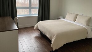 Ein Schlafzimmer mit Bett, Schreibtisch, einem Fenster mit Vorhängen und Blick auf Bäume.