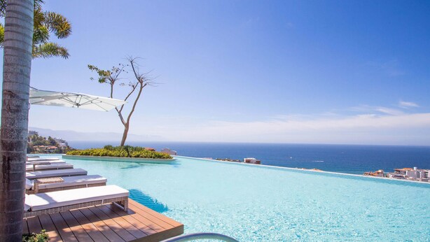 Zona de piscina con sillones de descanso y vista al océano.