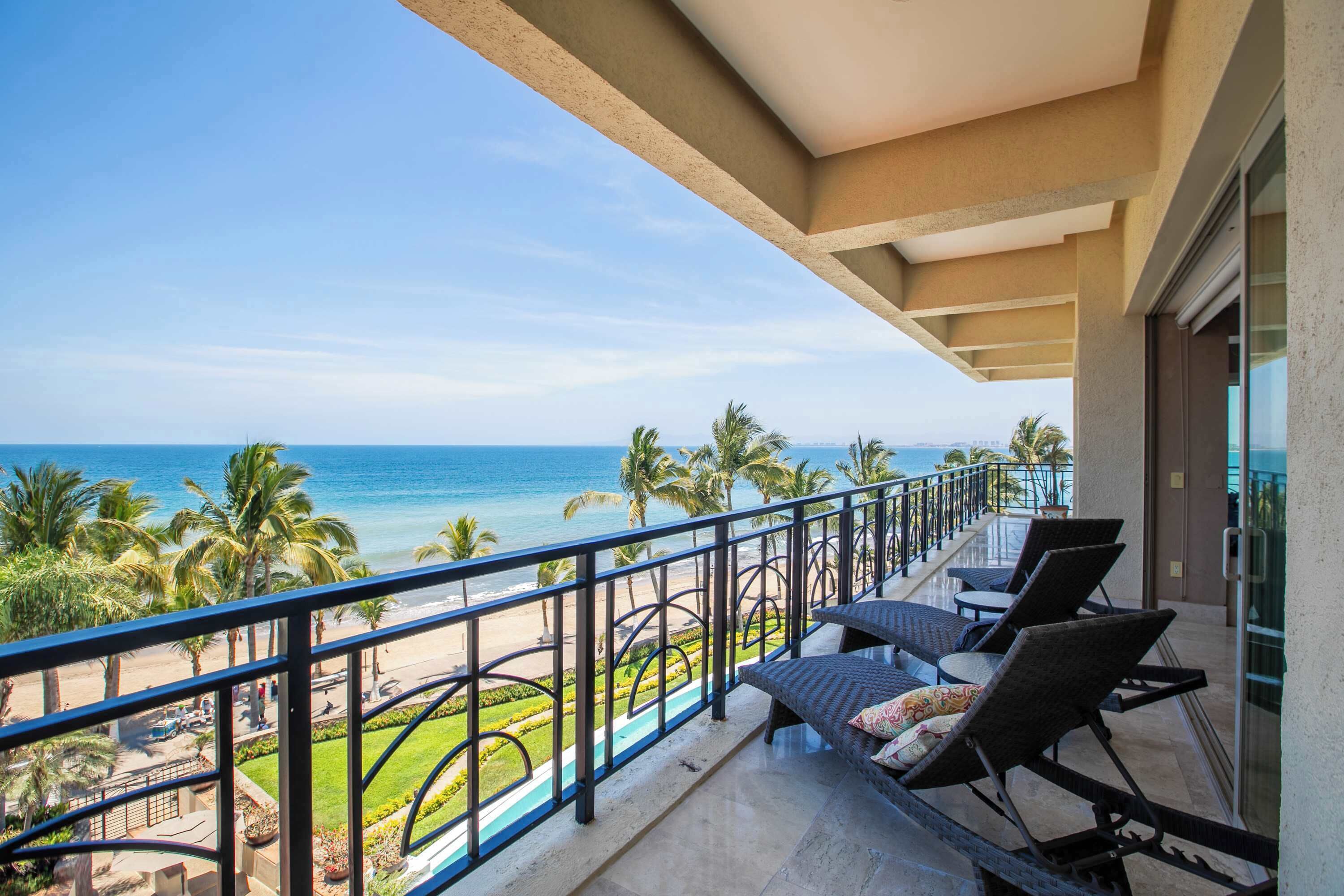 A balcony with a view of the beach and ocean, featuring lounge chairs and a railing.
