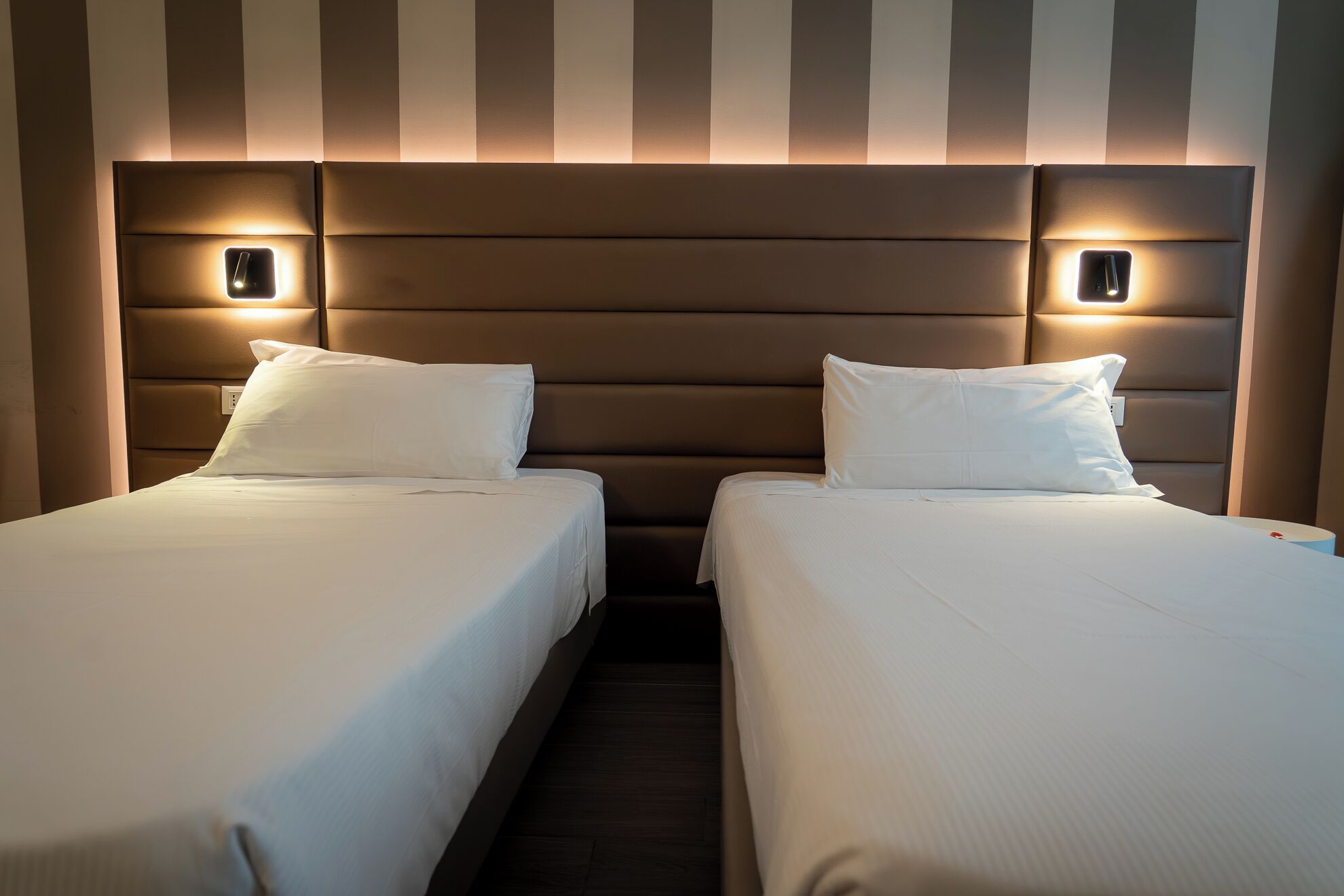 Hotellihuone, jossa on kaksi erillistä sänkyä, raidallinen seinä ja yöpöytävalaisimet.