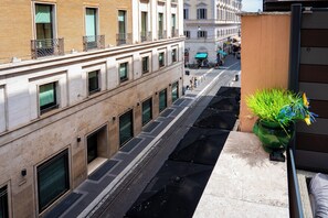 A narrow street with buildings on either side, a green plant on the right, and a visible shop sign. - RESIDENZA 62 (Rome)