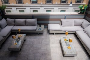 Terraza en la azotea con un área de estar exterior moderna, que incluye un sofá y dos mesas de centro con lámparas.