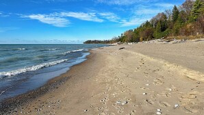 A beach with a pebbly shoreline, waves gently lapping at the sand, and a forested area in the background.