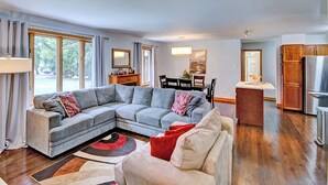 A spacious living room with a sectional sofa, a dining area, and a kitchen with wooden cabinets and a stainless steel refrigerator.