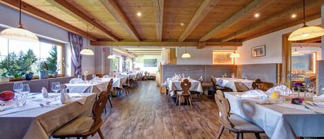 A restaurant with wooden beams, tables set with white tablecloths, and hanging pendant lights.