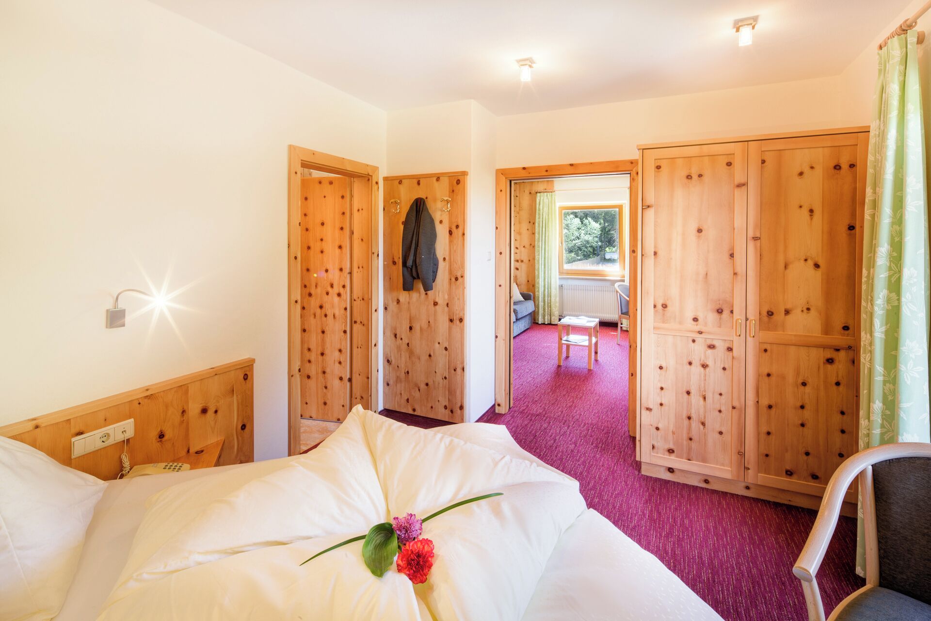 Habitación de hotel con cama, armario de madera, una mesita y vistas a un balcón exterior.