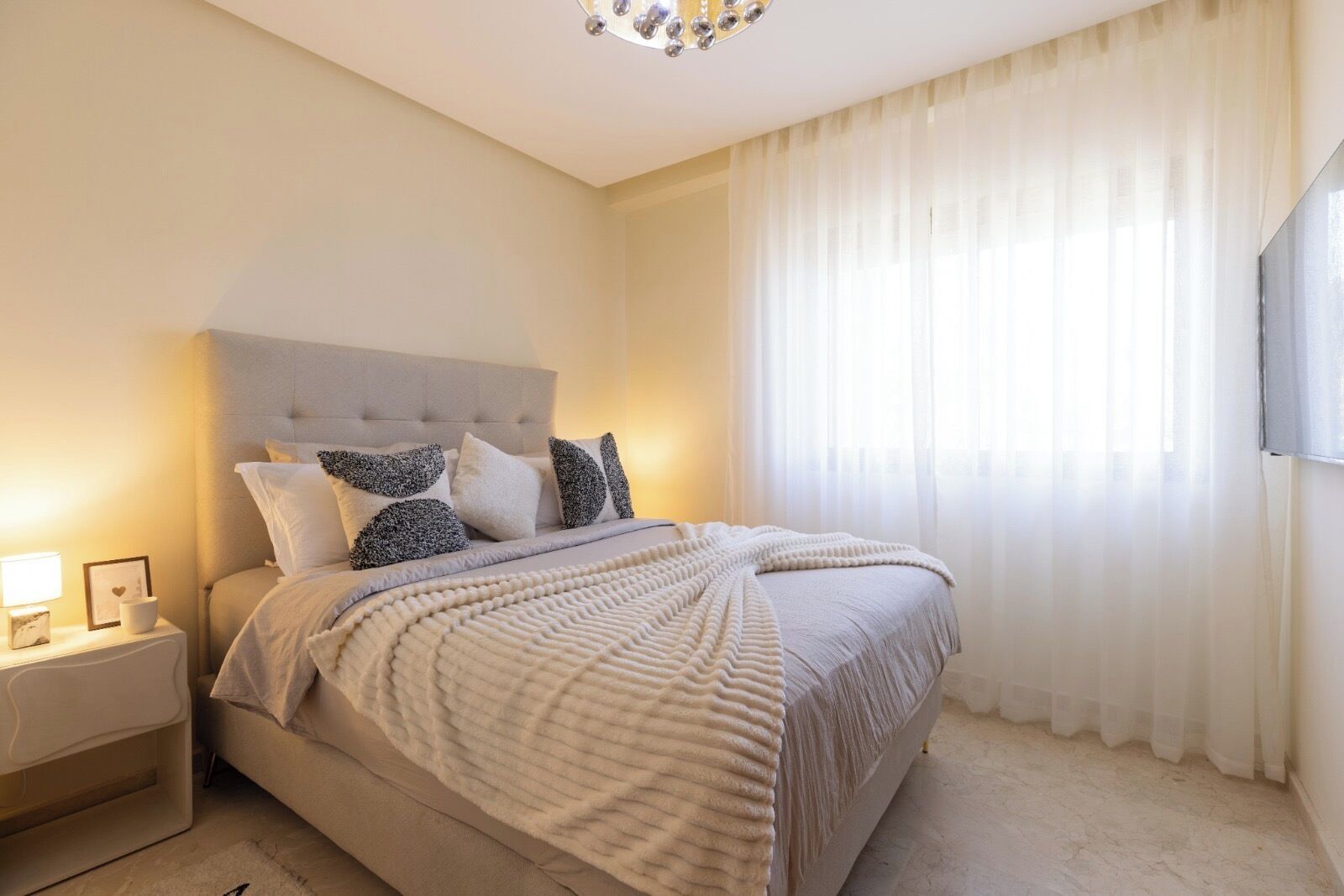 Ein Schlafzimmer mit einem Bett, einem Nachttisch, einer Lampe und einem Fenster mit Vorhängen.
