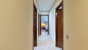 A narrow hallway with wooden doors on either side, leading to a bedroom with a bed and a nightstand. - Apartment Prestigia Agate - Golf view, Swimming pool & Comfort in Marrakech (Nîmes)
