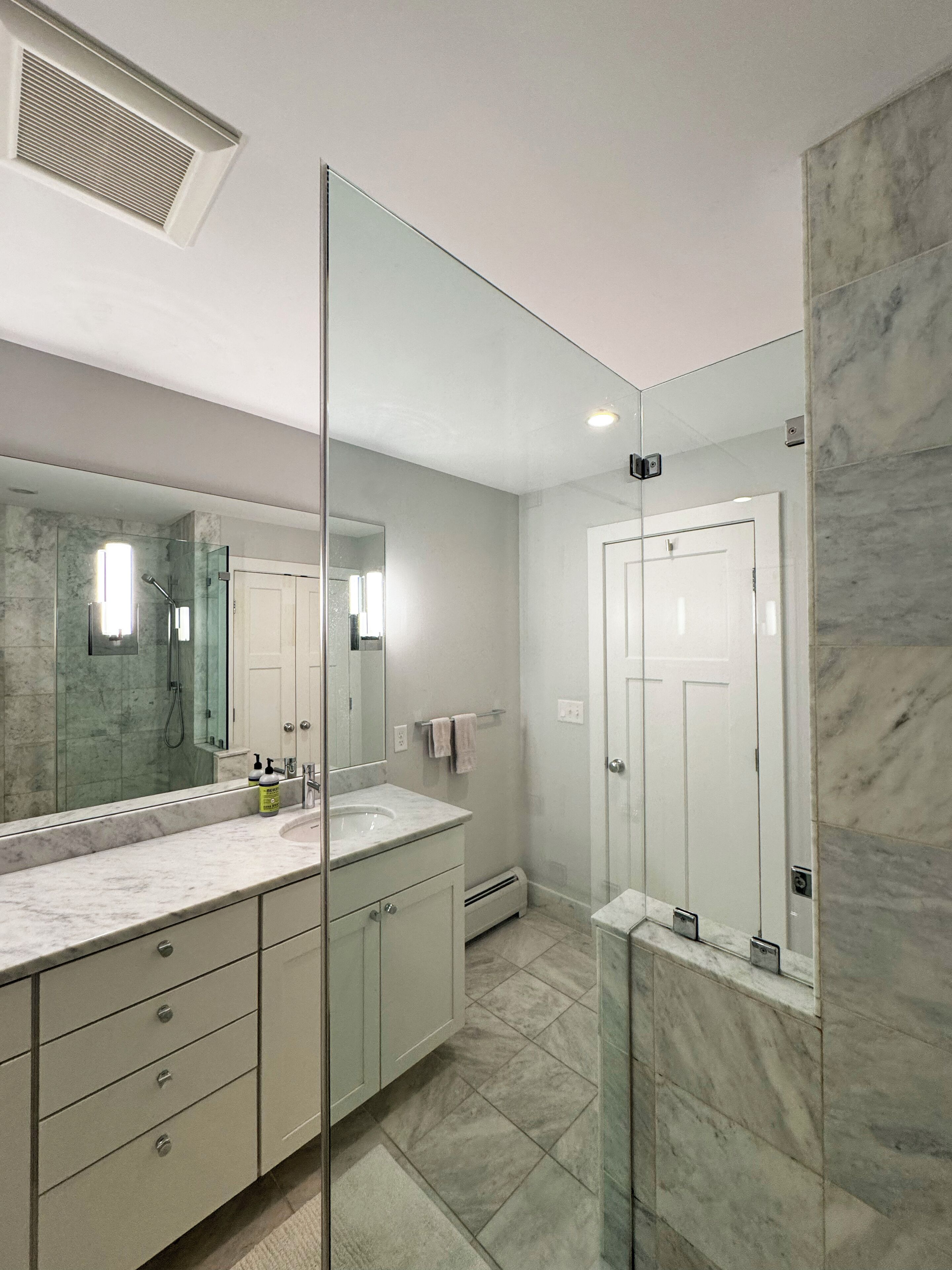 A modern bathroom with a glass partition, a marble sink, and a separate shower area.