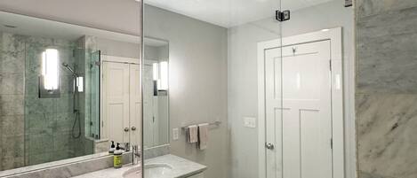 A modern bathroom with a glass partition, a marble sink, and a separate shower area.