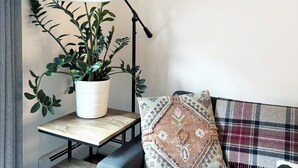 Een moderne woonkamer met een bank, bijzettafeltje met een plant in pot, een vloerlamp en een geruit plaid.