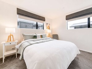 A modern bedroom with a large bed, bedside tables, and a window with blinds.