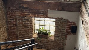 Un escalier avec une rampe en métal, des murs en briques et une fenêtre ornée d’une plante.