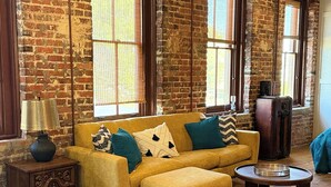 Un salon chaleureux avec un canapé jaune, une table basse en bois et un mur en briques.