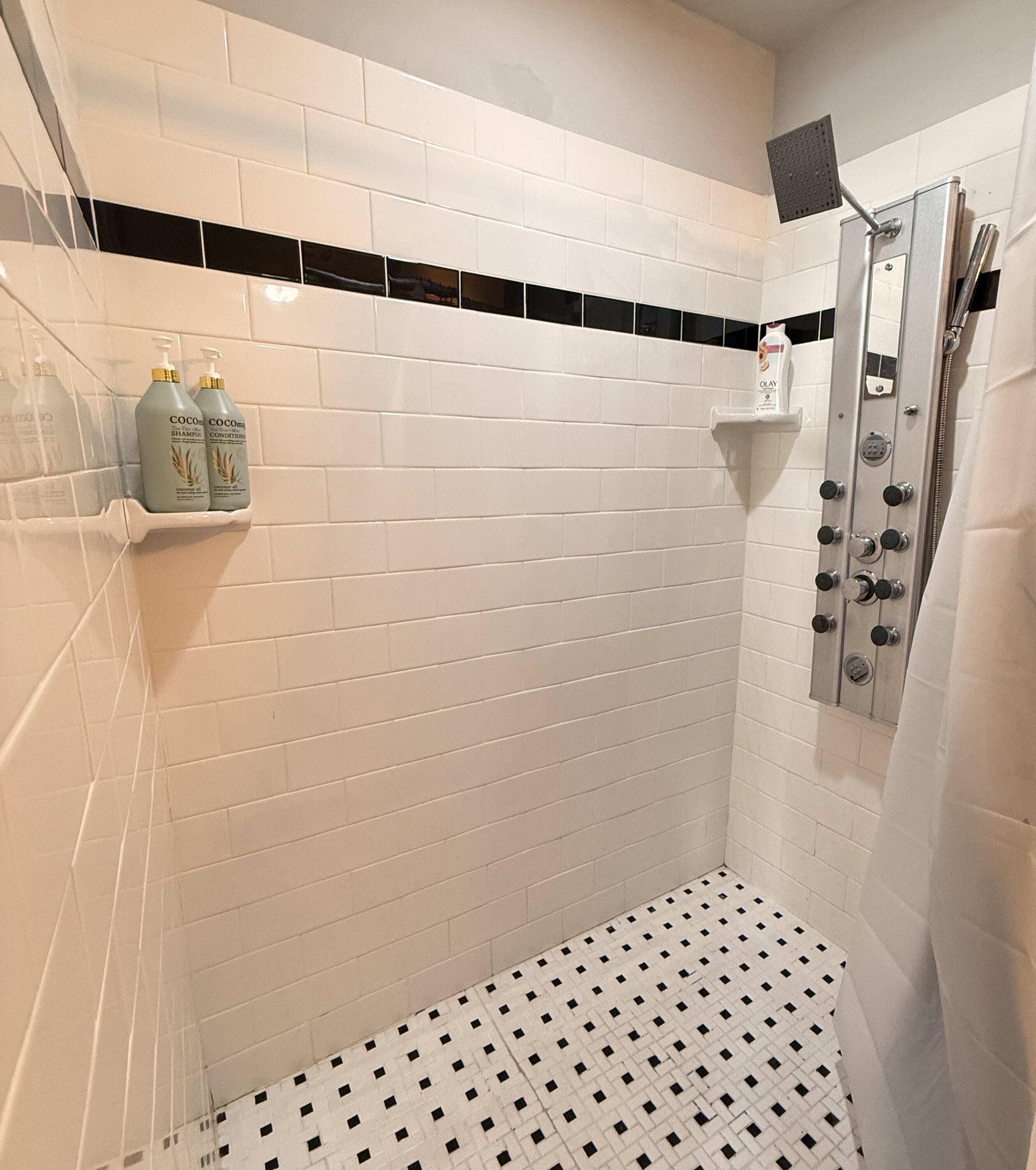 Ducha con azulejos blancos tipo metro, piso con estampado en blanco y negro, y estante con botellas de champú.