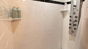 Ducha con azulejos blancos tipo metro, piso con estampado en blanco y negro, y estante con botellas de champú.