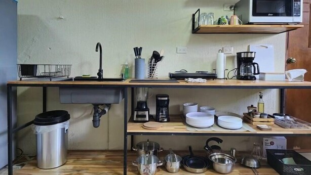 Una cucina compatta con lavandino, macchina del caffè e diversi utensili sul piano di lavoro.
