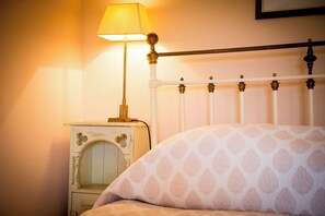 A bed with a patterned pillow, a bedside table with a lamp, and a metal headboard. - The Red Barn (Tavistock)