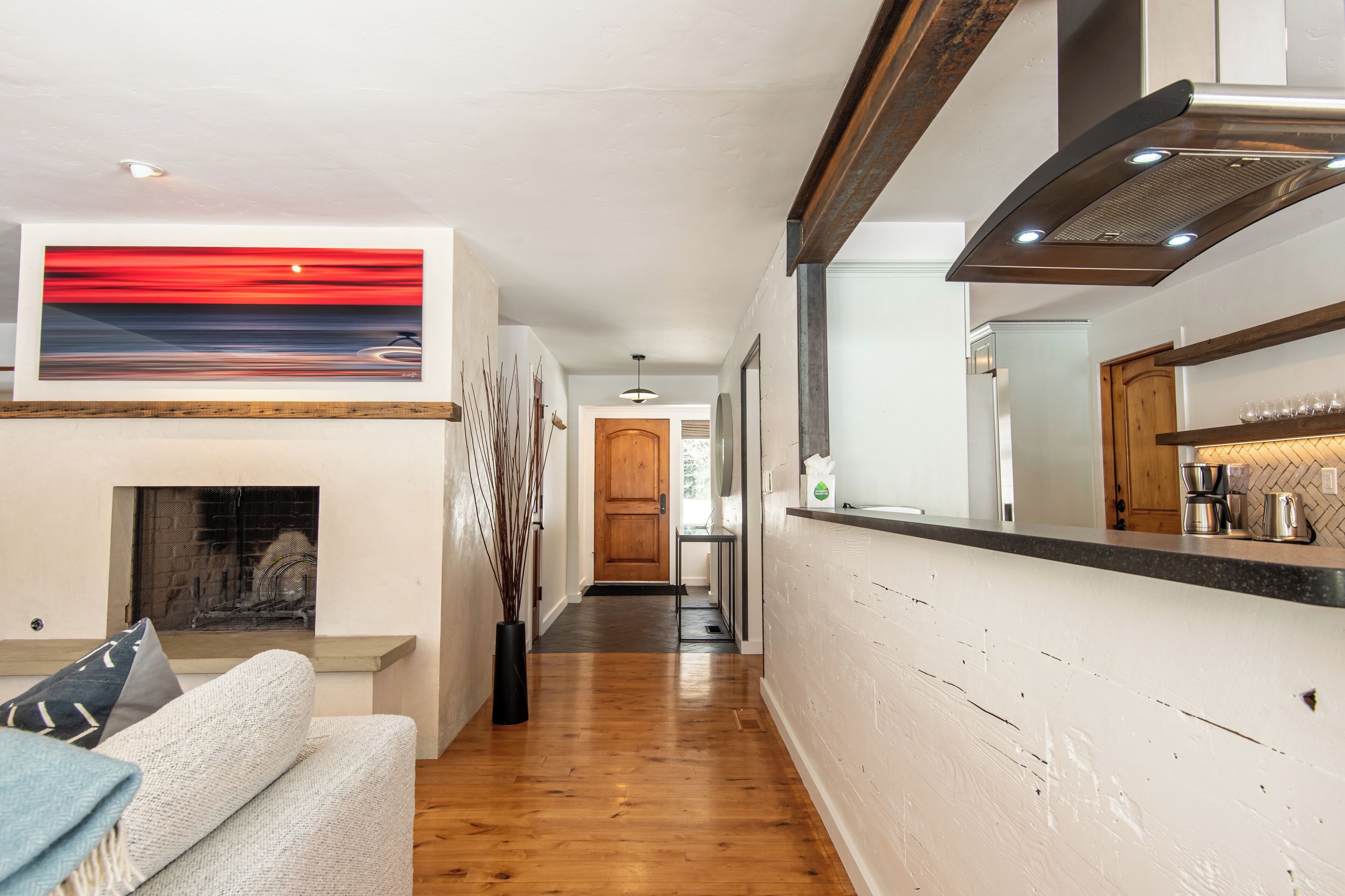 Un interior moderno con chimenea, una zona de cocina y un pasillo que lleva a una puerta de madera.