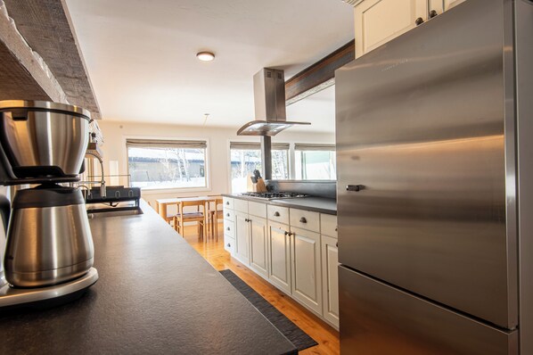 A modern kitchen with stainless steel appliances, wooden cabinets, and a large window providing a view of the outdoors.