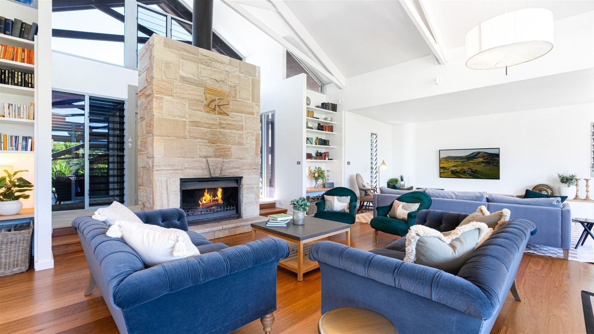 A modern living room with a stone fireplace, blue sofas, and a bookshelf.