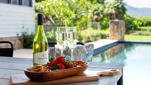 Une bouteille de vin, deux verres, des fraises et un bol de bretzels sur une table près d’une piscine.