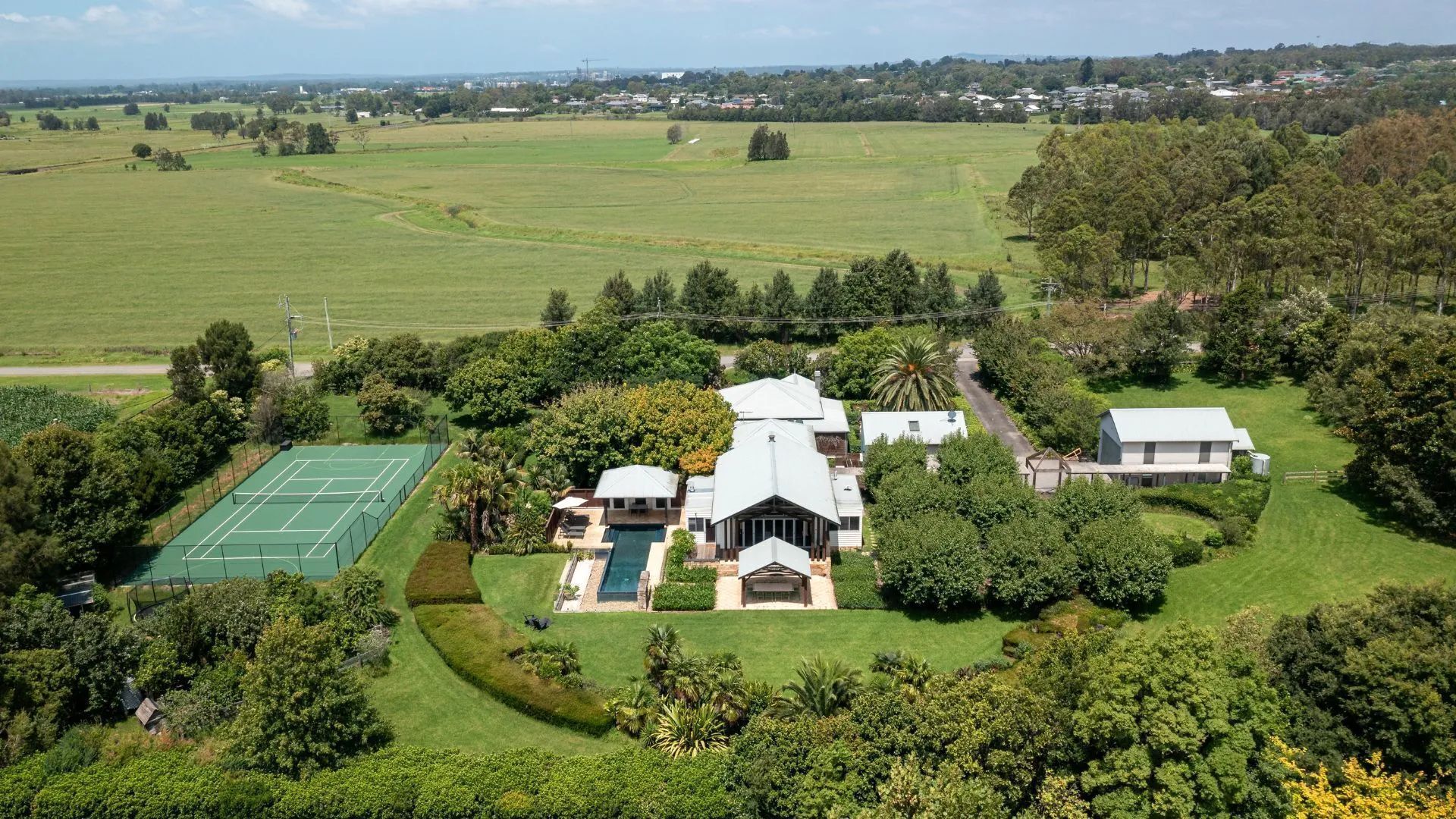 A large estate with a tennis court, swimming pool, and multiple buildings surrounded by lush greenery.