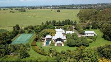A large estate with a tennis court, swimming pool, and multiple buildings surrounded by lush greenery.