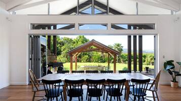 A spacious dining area with a large table and chairs, a wooden pergola, and a view of a lush garden and mountains.