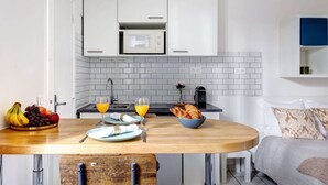 A modern kitchen with white cabinets, a microwave, and a breakfast setup including fruits, croissants, and orange juice. - Charming Studio near Eiffel Tower for 2 (Paris)