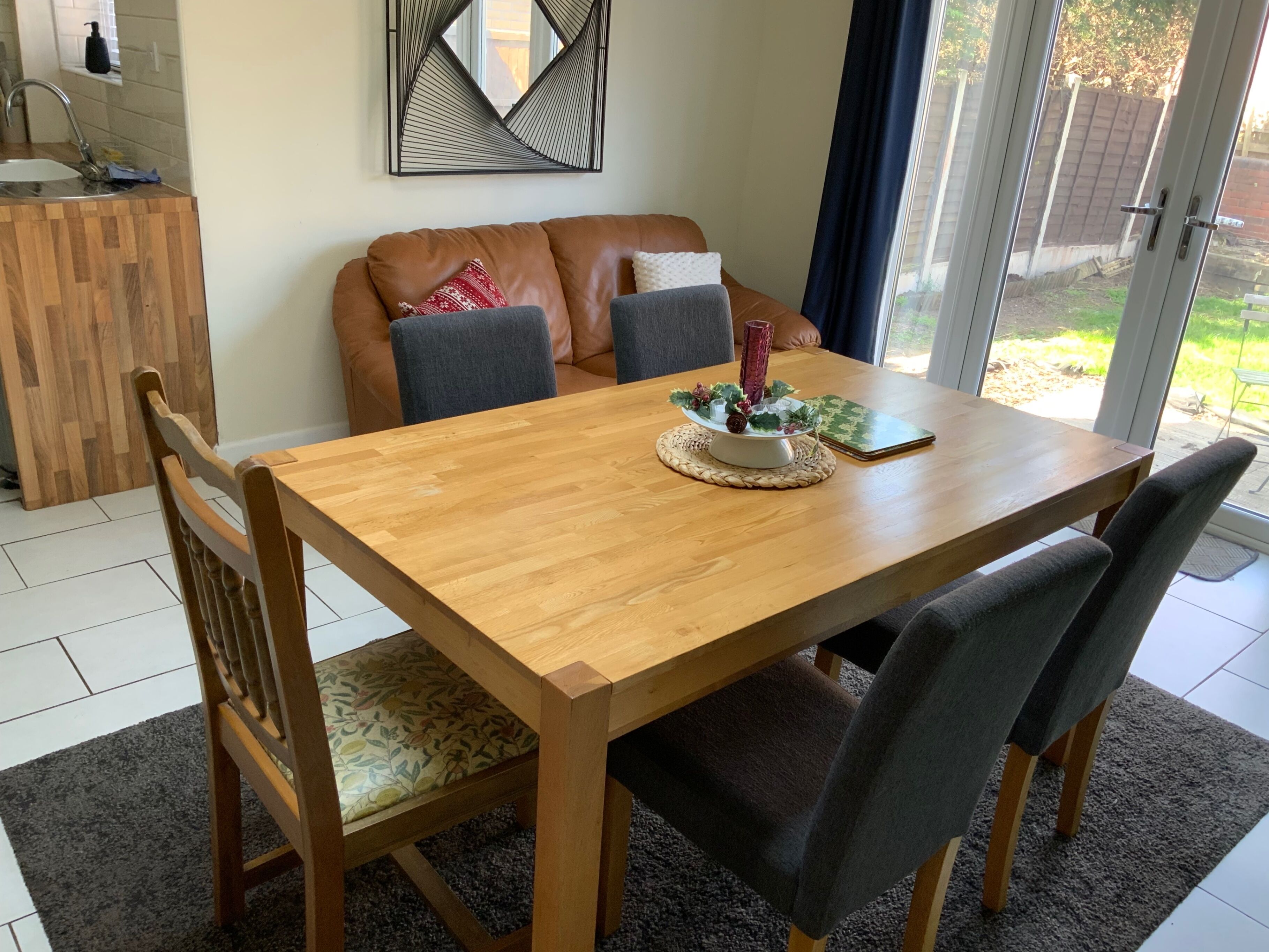 Un coin repas avec une table en bois, quatre chaises, un élément décoratif au centre de la table et une vue à travers une porte vitrée.