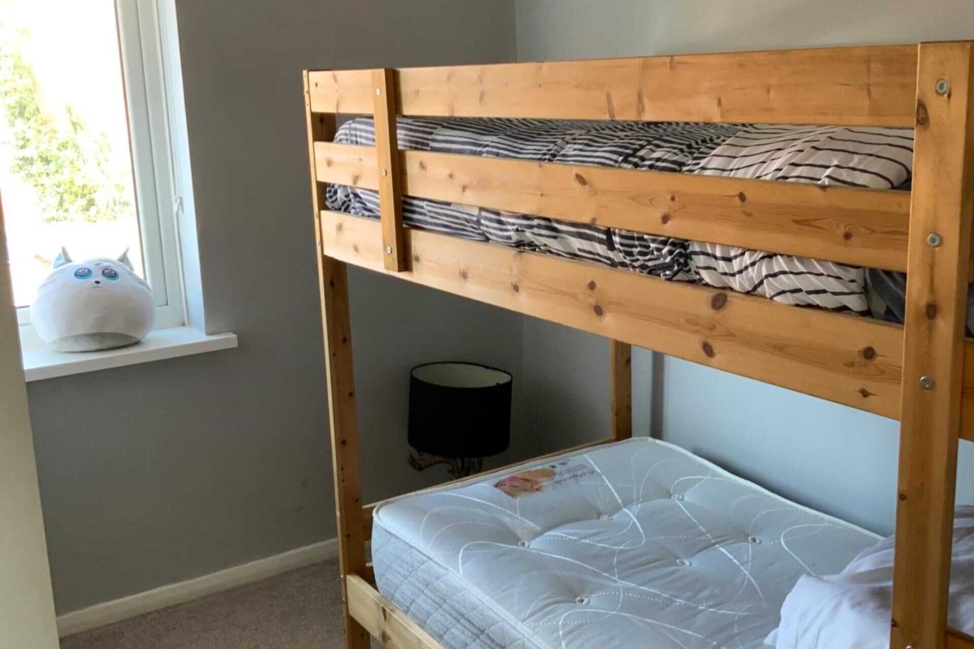 A bunk bed with a mattress and pillows, a window with a view, and a small table with a plush toy.