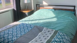 Ein Schlafzimmer mit einem Bett, einem Nachttisch mit Lampe, einem Fenster und einer Heizung.