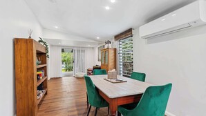 A dining area with a wooden table and green chairs, a wooden bookshelf, and an air conditioning unit. - Tropical Family Retreat with Pool and Garden (Machans Beach)
