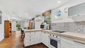 A modern kitchen with white cabinetry, a built-in microwave, and a large window with a view of greenery. - Tropical Family Retreat with Pool and Garden (Machans Beach)