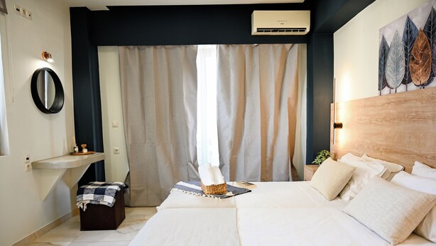 A hotel room with a bed, bedside table, and a wall-mounted air conditioner. - Cozy Studio 2 (Malia)