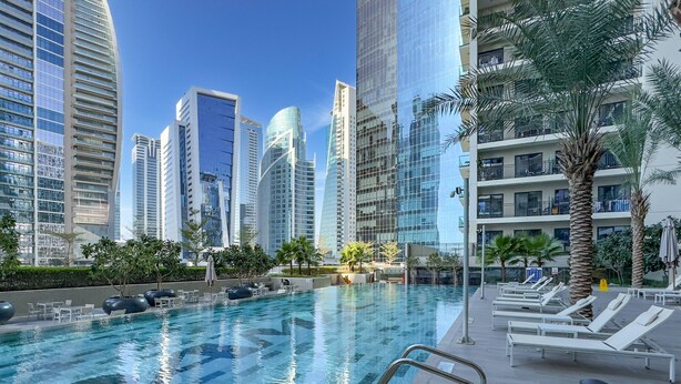A swimming pool with lounge chairs and palm trees, surrounded by high-rise buildings.