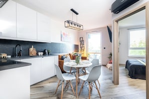 Cozinha moderna com armários brancos, bancada preta e área de jantar com mesa e cadeiras redondas.