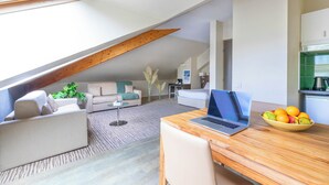 A modern living room with a sloped ceiling, a wooden dining table with a laptop, a bowl of fruit, and a sofa. - Secure downtown studio with hotel services Pets welcome (Chambéry)