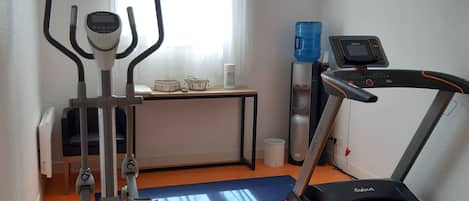 Gimnasio con una elíptica, una cinta de correr y un dispensador de agua.