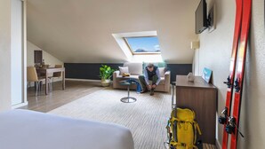 A room with a sloped ceiling, a skylight, a sofa, a dining table, chairs, a yellow backpack, and red skis leaning against the wall. - Secure downtown studio with hotel services Pets welcome (Chambéry)