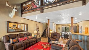 A spacious living room with a large brown sofa set, a red patterned rug, and a mounted deer head on the wall. - Summer Resort Access, Hiking/Fishing, Hot Tub/Pool! (Durango)
