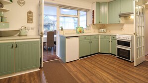 A kitchen with green cabinets, a white stove, and a window overlooking a garden. - Crown Farm (Wisbech)